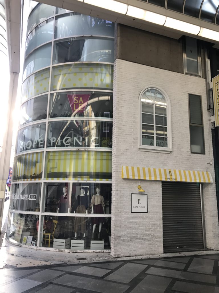 曲面ガラスから淡色タイルの側壁へ回り込む心斎橋TOの外観 / Exterior of Shinsaibashi TO where the curved glass facade turns toward the light-colored tiled side wall