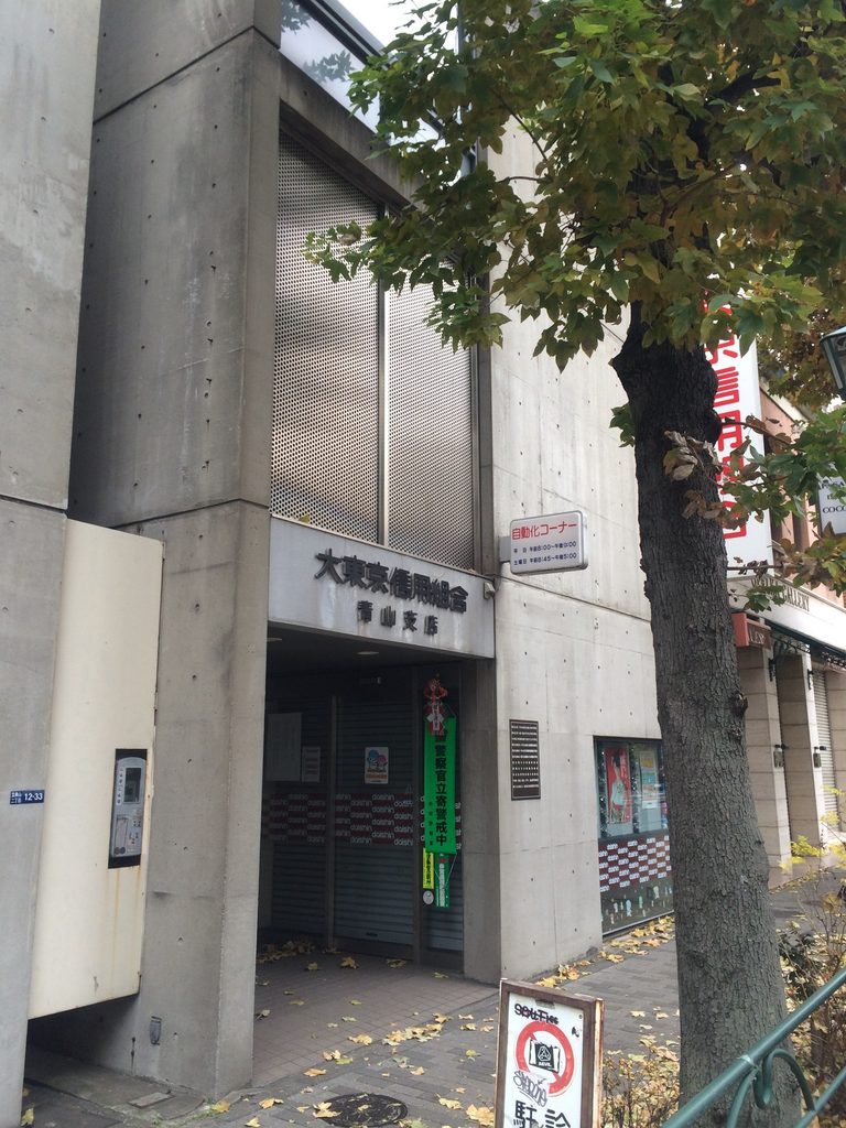 街路樹越しに見る青山TOの入口と打放しコンクリートの立面 / Entrance and exposed-concrete elevation of Aoyama TO seen through a street tree