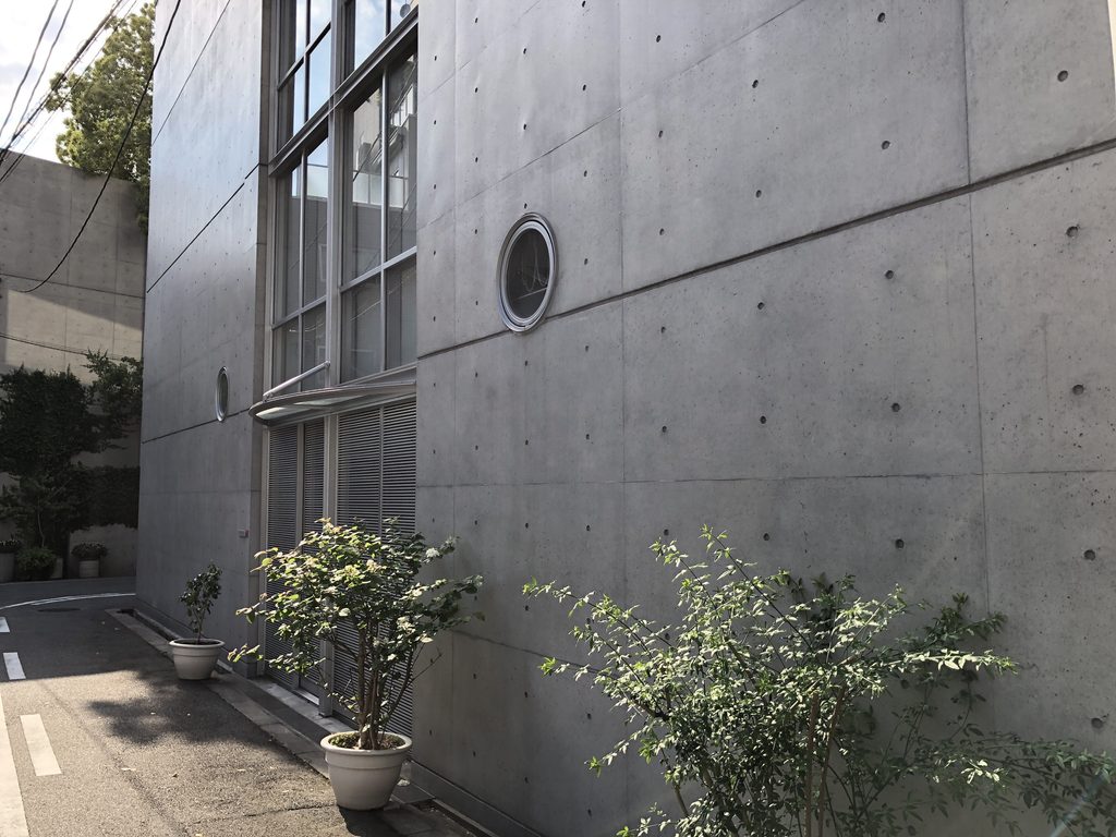 打放しの壁に開く丸窓と足元の鉢植え / Round window in the concrete wall with potted plants below