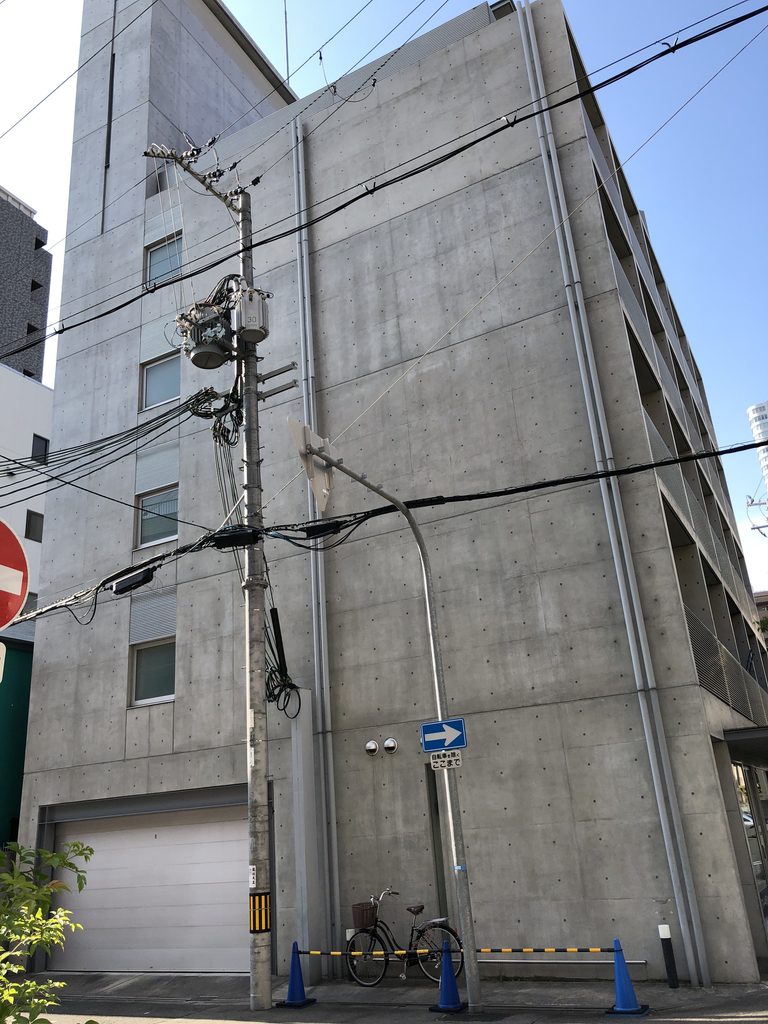 小さな開口とシャッターを持つ背の高い打放しの立面 / Tall exposed-concrete elevation with small openings and a shutter