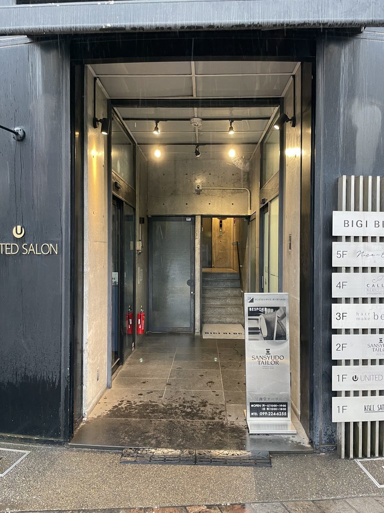 打放しコンクリート壁の間を上るBIGIビルの共用階段 / Shared stair rising between exposed-concrete walls inside BIGI Building