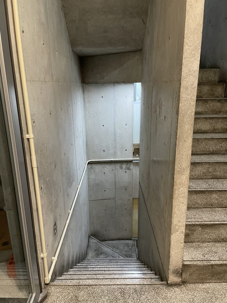 街路の光へ向かって伸びるBIGIビルのコンクリート通路 / Concrete passage inside BIGI Building leading toward daylight from the street