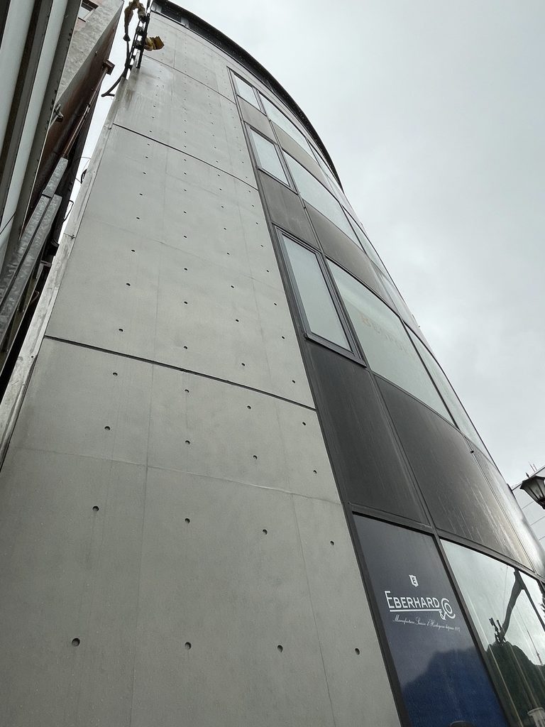 下から見上げるBIGIビルの曲面外壁と最上部のコンクリートボリューム / Upward view of BIGI Building showing its curved facade and upper concrete volume