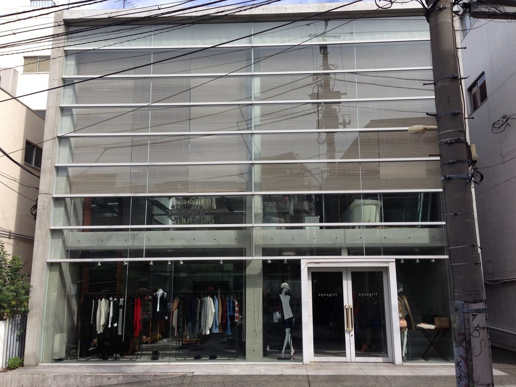COCUEの正面を覆うガラスファサードと両側の打放しコンクリート壁 / Full glazed street facade of COCUE framed by exposed-concrete side walls