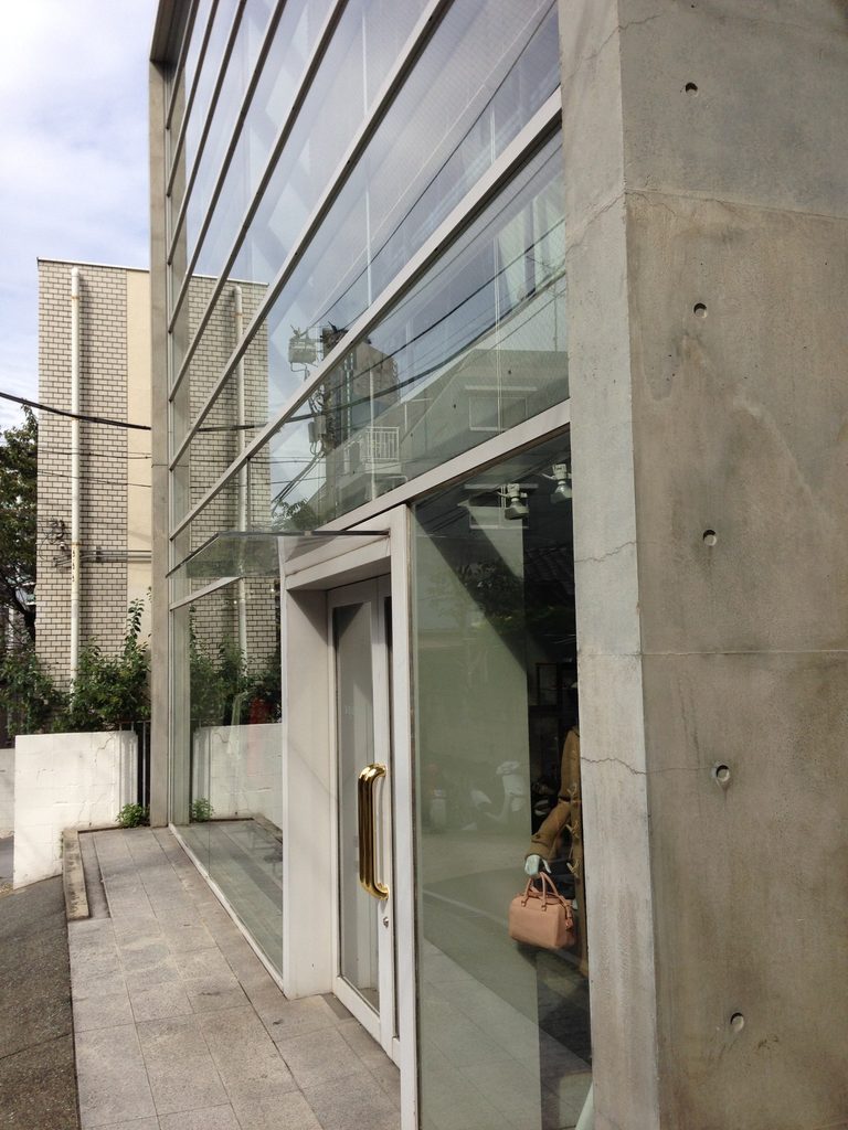 COCUEのガラスファサードに設けられた入口と打放しコンクリート壁 / Entrance set within COCUE's glazed facade beside an exposed-concrete wall