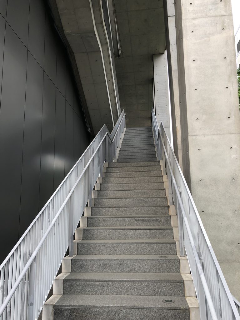 柱と金属の壁の間を上る細い階段 / Narrow stair rising between a column and metal-clad wall