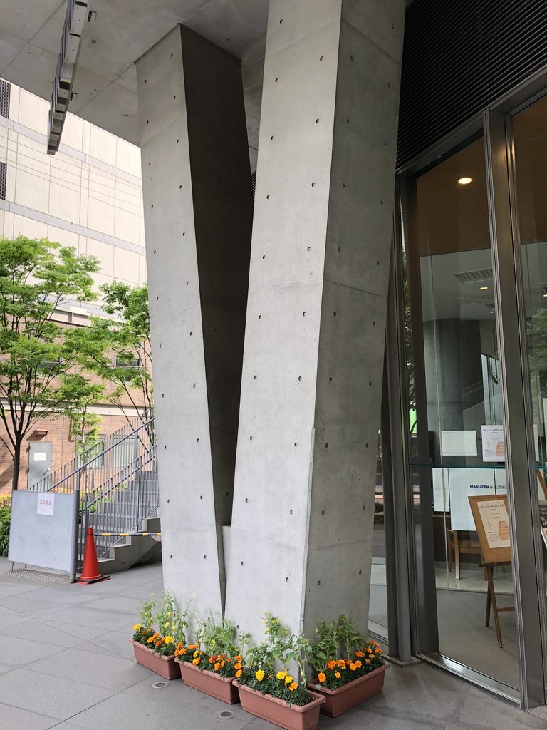 一点で接する二本のV字柱と足元の花 / Two V-shaped columns meeting at a point with flowers at their base