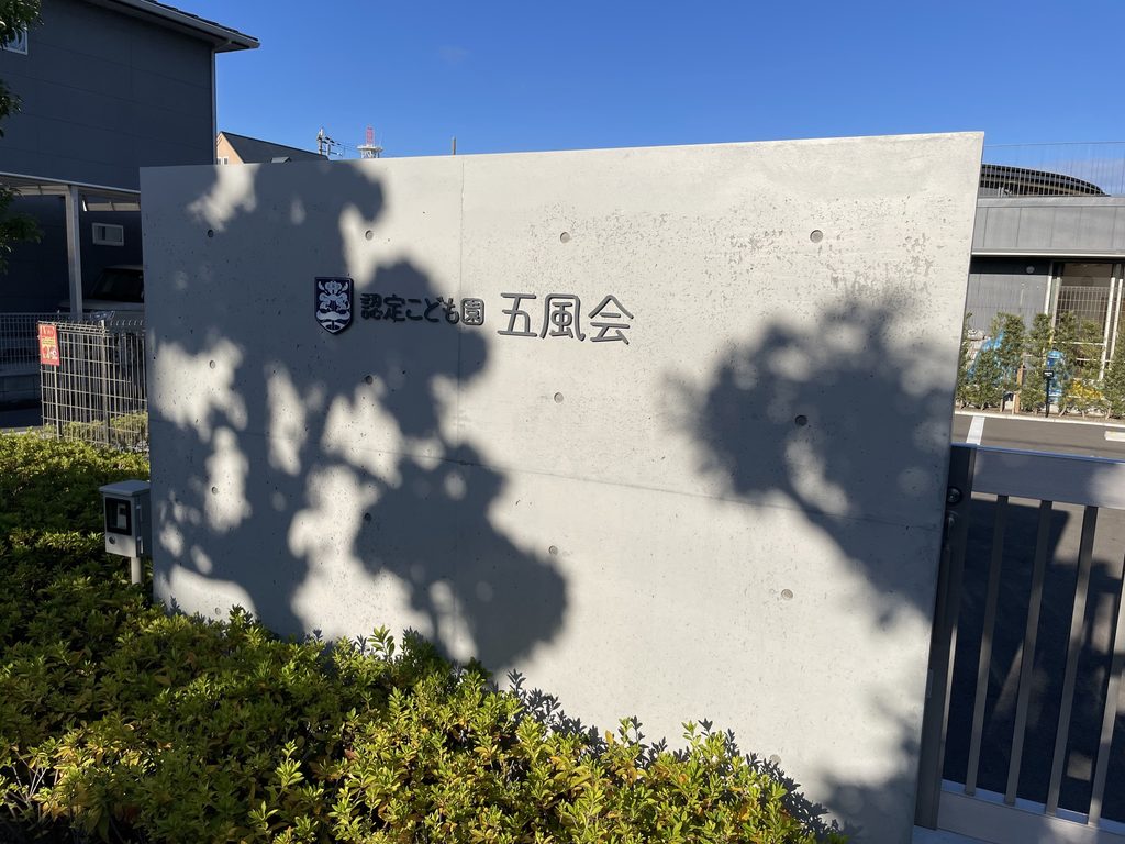 植栽の影が落ちる五風会の打放しコンクリートのサイン壁 / Exposed-concrete sign wall of Gofukai with shadows from surrounding planting