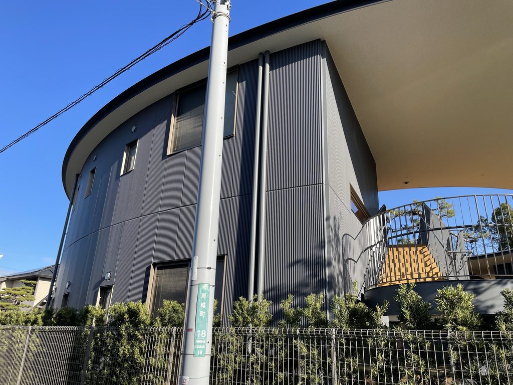 緩やかに湾曲する濃色の外壁と円形屋根を見上げた五風会 / Curving dark exterior wall and circular roof of Gofukai seen from below