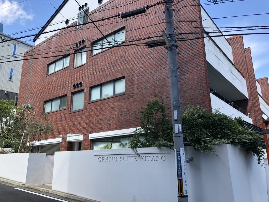 坂道から見るグランスイート北野の赤レンガ外壁と白い塀 / Red-brick exterior and white boundary wall of Grand Suite Kitano viewed from the sloping street