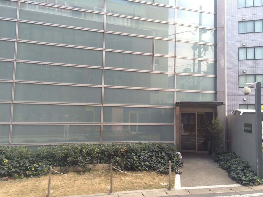 植栽と低いコンクリート壁に囲まれた橋本眼科西口医院の入口側外観 / Entrance side of Hashimoto Eye Clinic framed by planting and low concrete walls