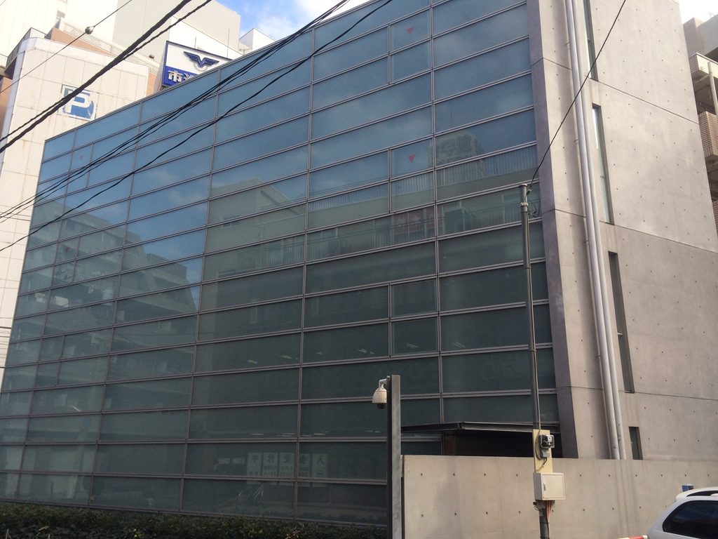 半透明のガラス面とコンクリート壁を斜めから見る橋本眼科西口医院 / Oblique view of Hashimoto Eye Clinic showing translucent glazing and concrete wall