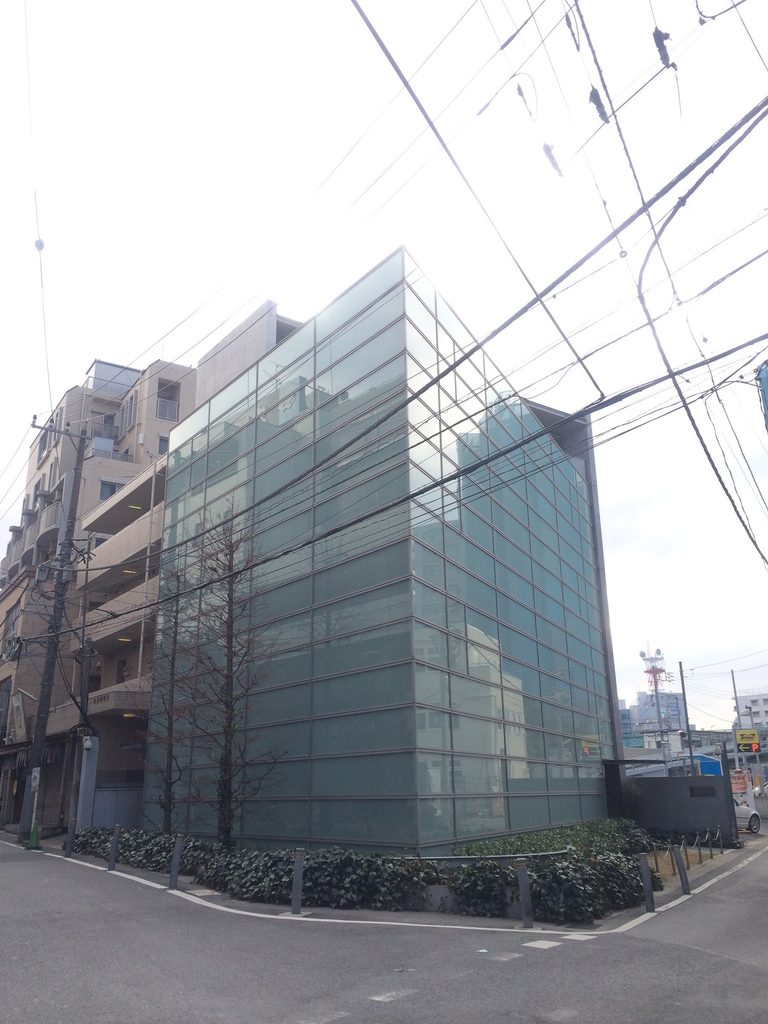 街角から見る橋本眼科西口医院の二方向に広がるガラス外壁 / Corner view of Hashimoto Eye Clinic with glazed facades extending in two directions