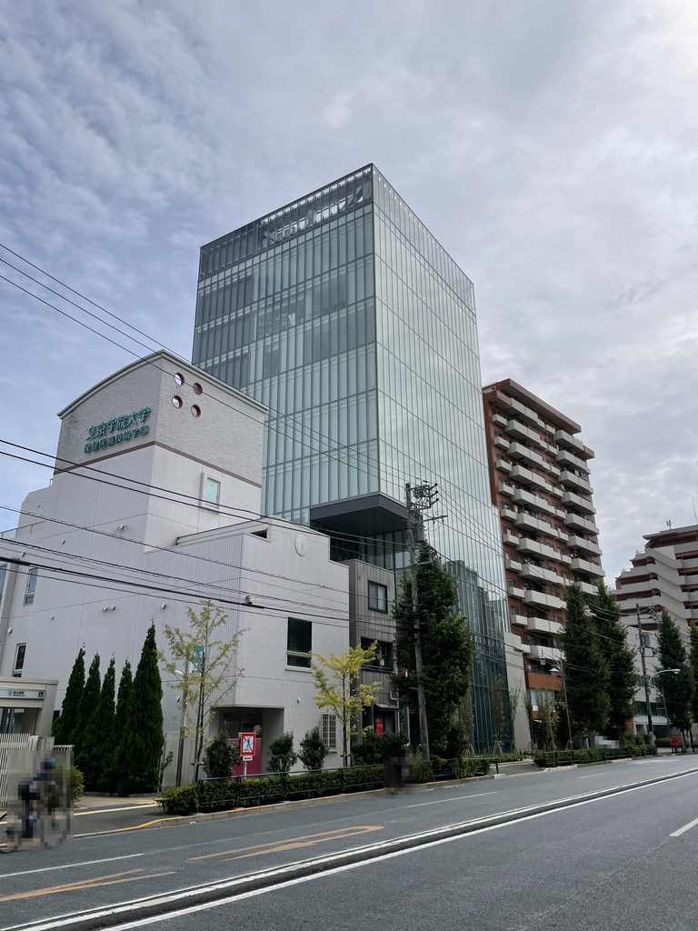 低層建築の上に立ち上がるHiRAKU GATEのガラスの塔 / Glass tower of HiRAKU GATE rising above a lower building