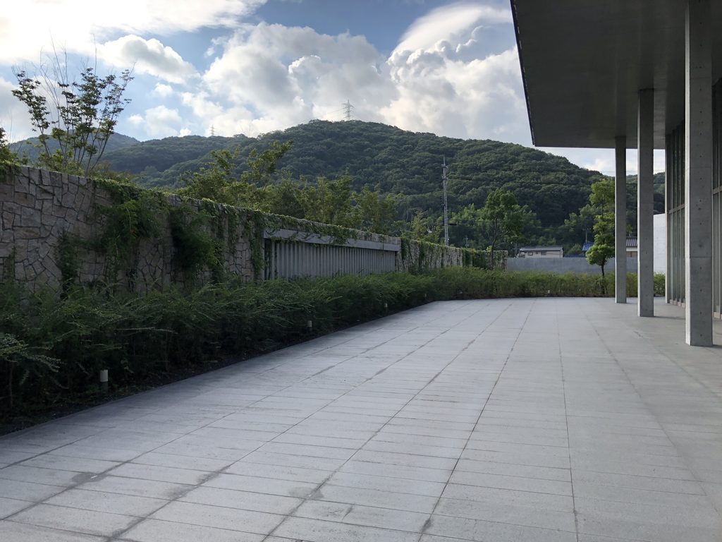 列柱廊の先に広がる舗装面と岡山の山並み / Paved space and mountain landscape beyond the colonnade