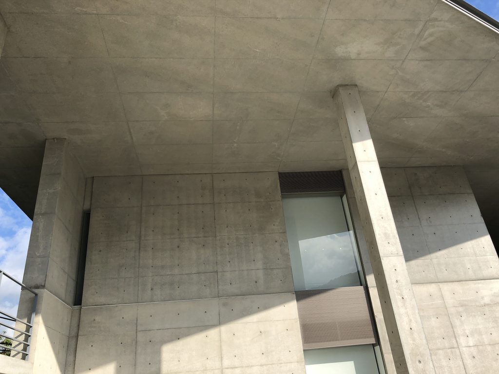 深い軒下に続く打放しコンクリートの柱と影 / Concrete columns and deep shadows beneath the projecting roof
