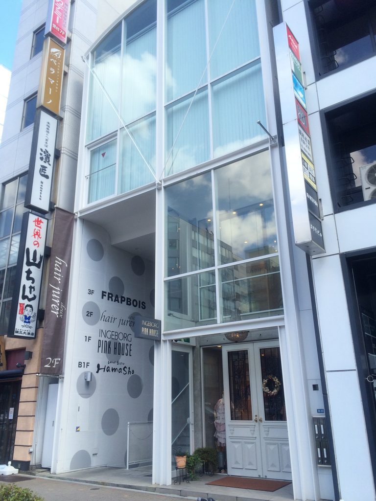 街路から見上げるJ ROOMのガラス外観と縦長の構成 / Glazed exterior and narrow vertical composition of J ROOM viewed from the street