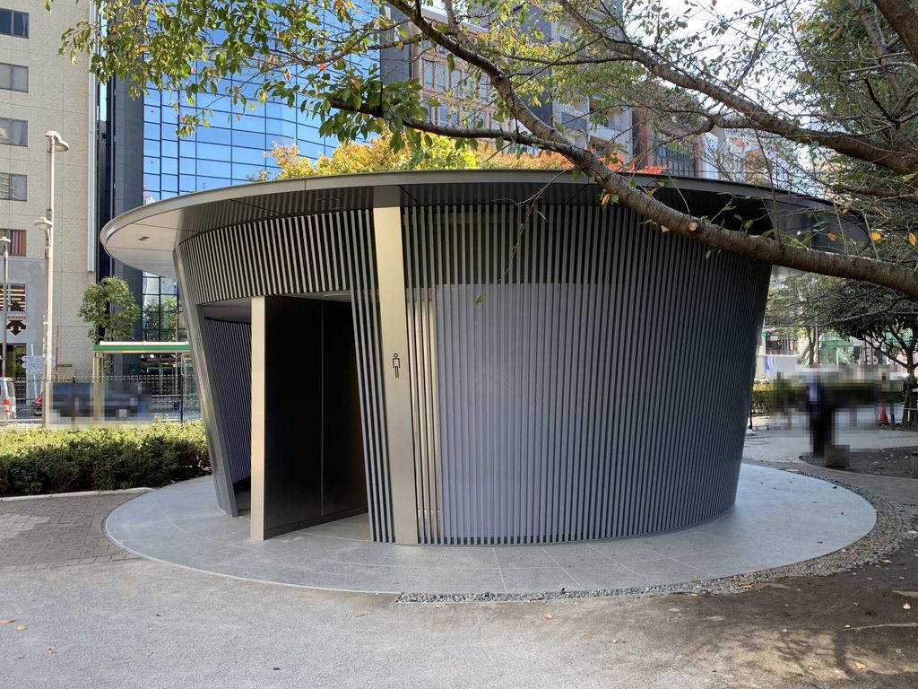 円形の足元に立つ縦格子の外壁と円盤状の屋根 / Vertical-louver enclosure and disc-like roof rising from the circular paved area