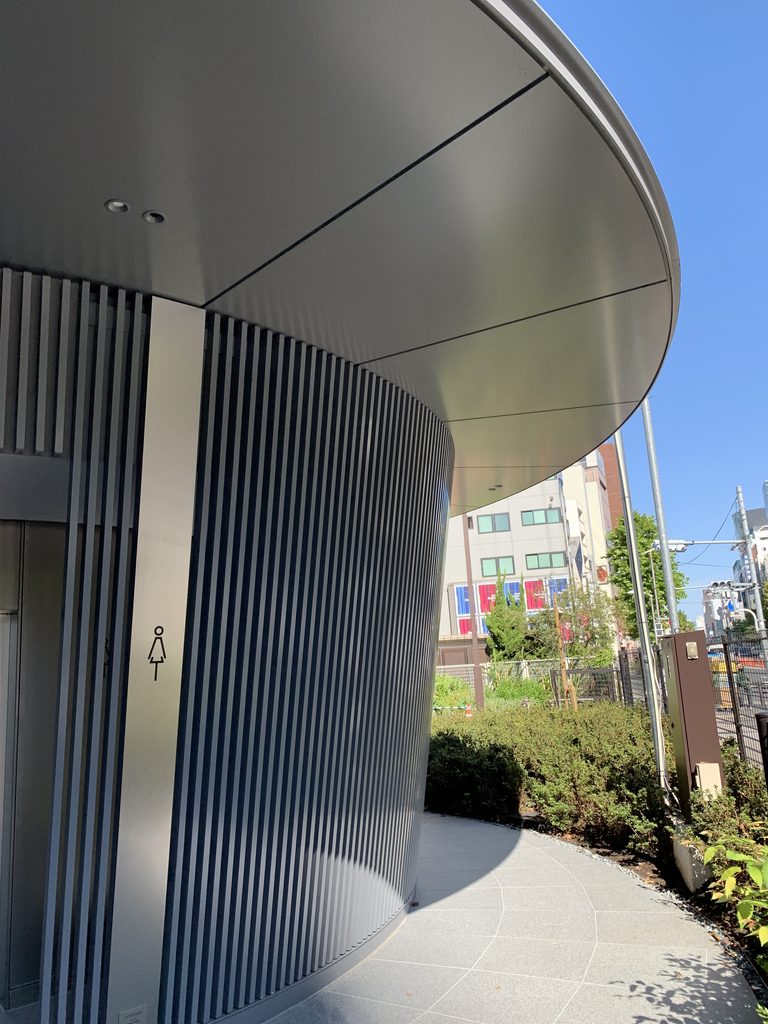 縦格子の外壁から円弧を描いて張り出す薄い庇 / Thin curved eaves projecting beyond the vertical-louver enclosure