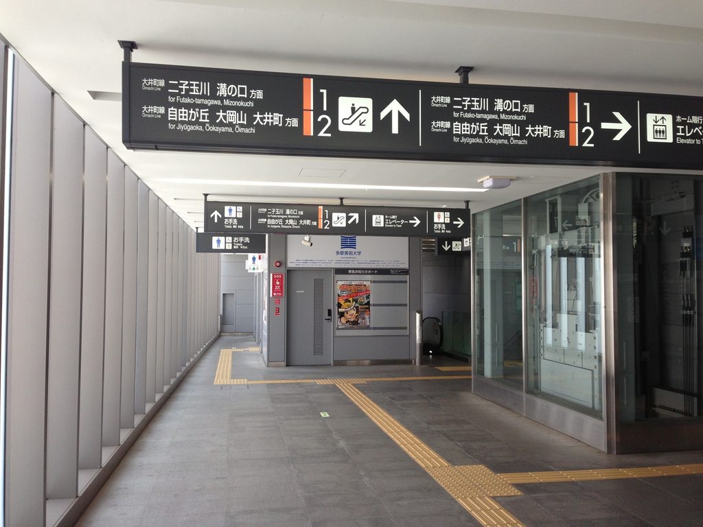 半透明の壁面と誘導ブロックが奥へ続く上野毛駅コンコース / Kaminoge Station concourse with translucent walls and tactile paving extending into the distance