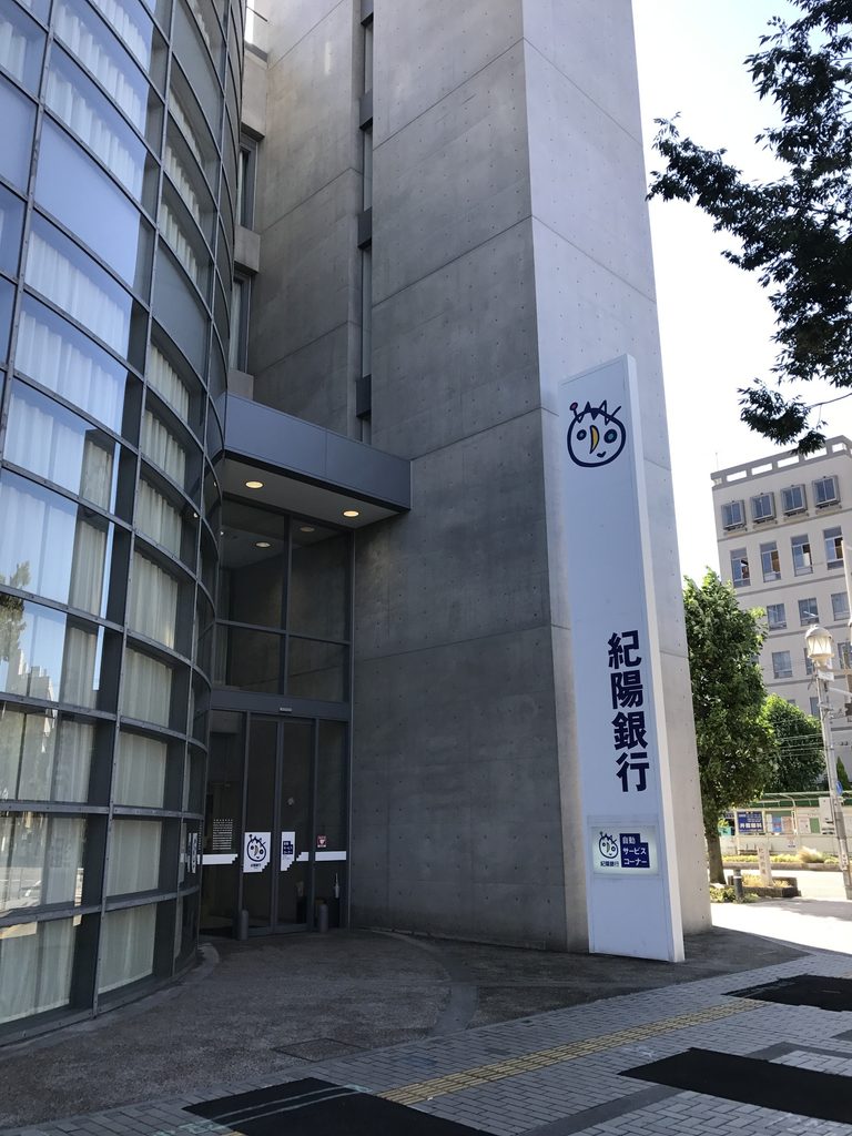 曲面ガラスと打放しコンクリートの間に設けられた紀陽銀行堺支店の入口 / Entrance to Kiyo Bank Sakai set between the curved glazing and exposed-concrete wall