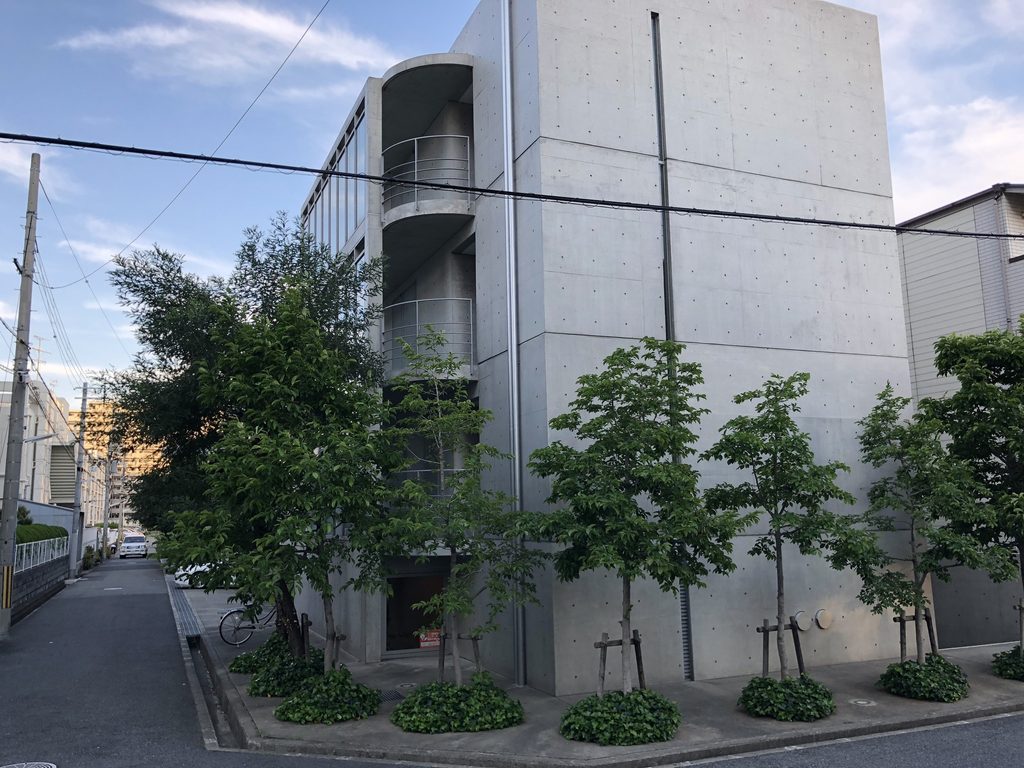 円弧状のバルコニーと大きなコンクリート壁が並ぶマグノリアの妻面 / Curved balconies beside the broad exposed-concrete end wall of MAGNOLIA