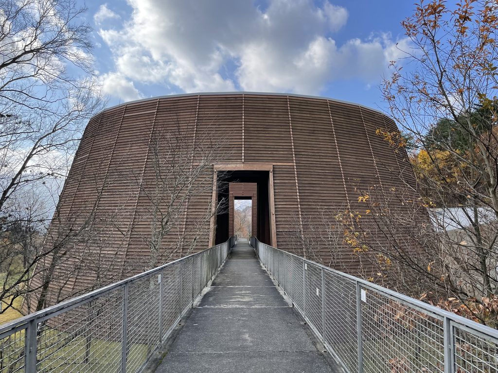 直線のアプローチ正面に現れる木の殿堂の円形外観 / Circular Museum of Wood seen at the end of its straight approach