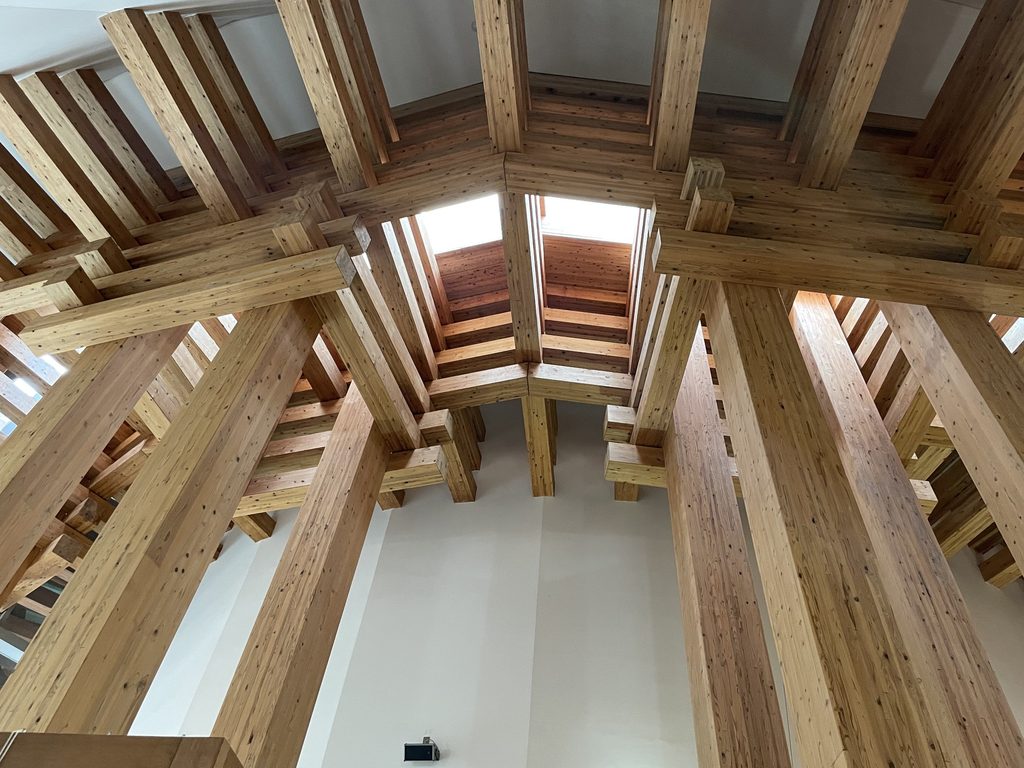 木の殿堂内部で頭上へ伸びる集成材の柱と梁 / Laminated timber columns and beams rising inside the Museum of Wood