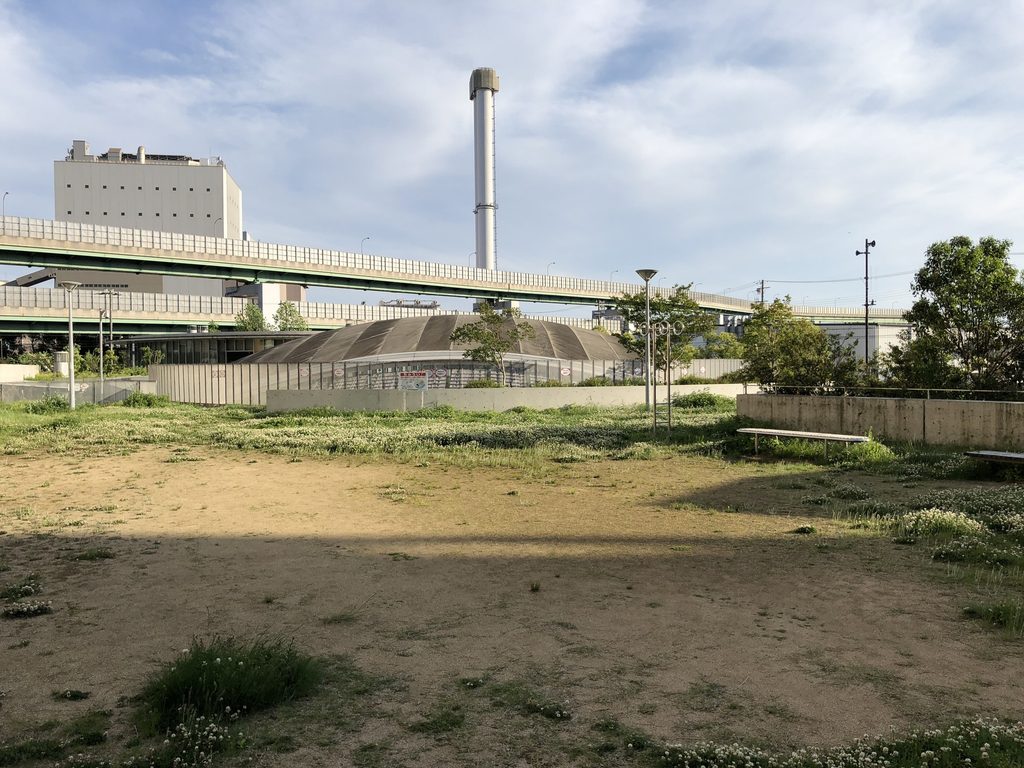 高架道路と工業施設を背景にした新在家南公園の開放的な地表面 / Open landscape of Shinzaike Minami Park with elevated roadway and industrial structures beyond