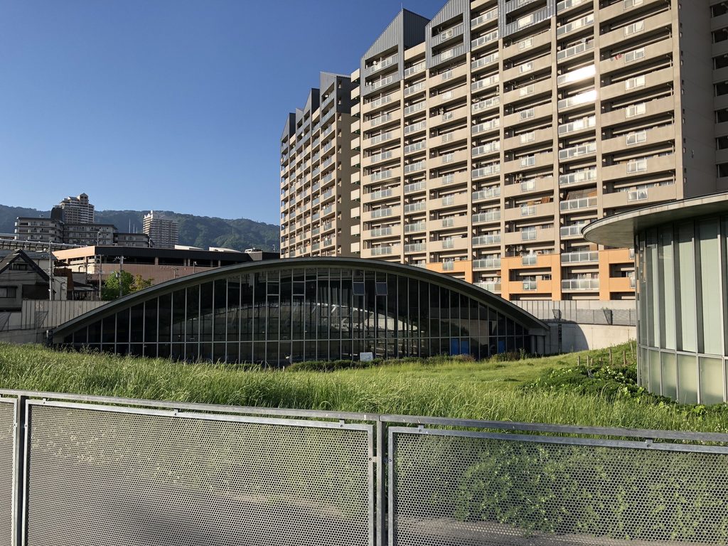 地面から弧を描いて立ち上がる灘浜ガーデンバーデンの低い楕円形ガラス屋根 / Low elliptical glazed roof of Nadahama Garden Baden rising in an arc from the landscape