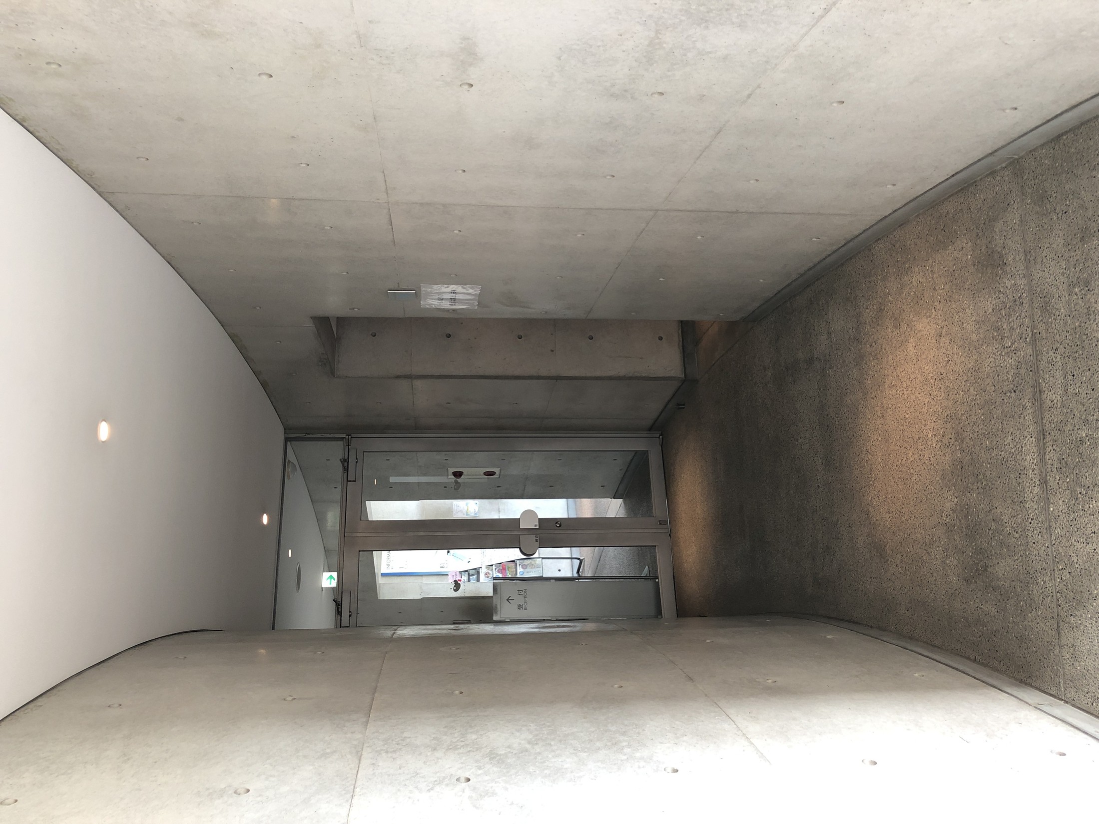 半地下へ続く打放しコンクリートの細長い通路空間 / Long exposed-concrete passage leading through the semi-subterranean level