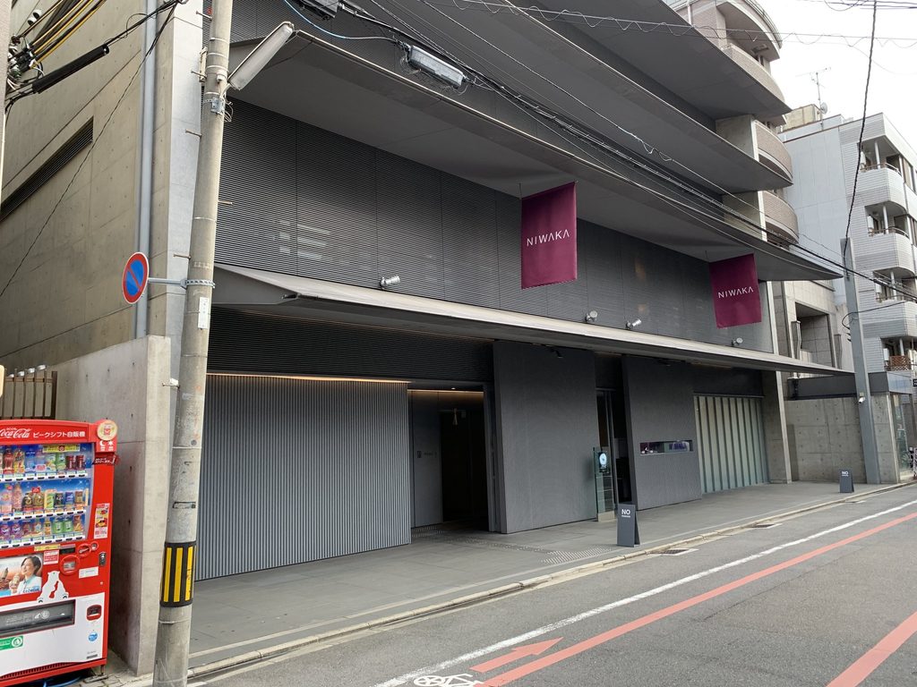 深い庇の下にNIWAKAの旗が並ぶ俄ビルの正面 / Street facade of the NIWAKA Building with NIWAKA banners beneath the deep eave