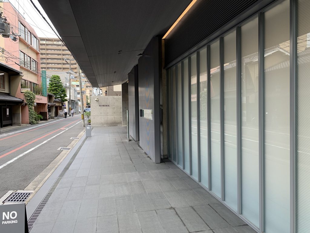 ガラス外壁に沿って続く俄ビルの庇下空間 / Space beneath the NIWAKA Building eave extending alongside the glazed facade