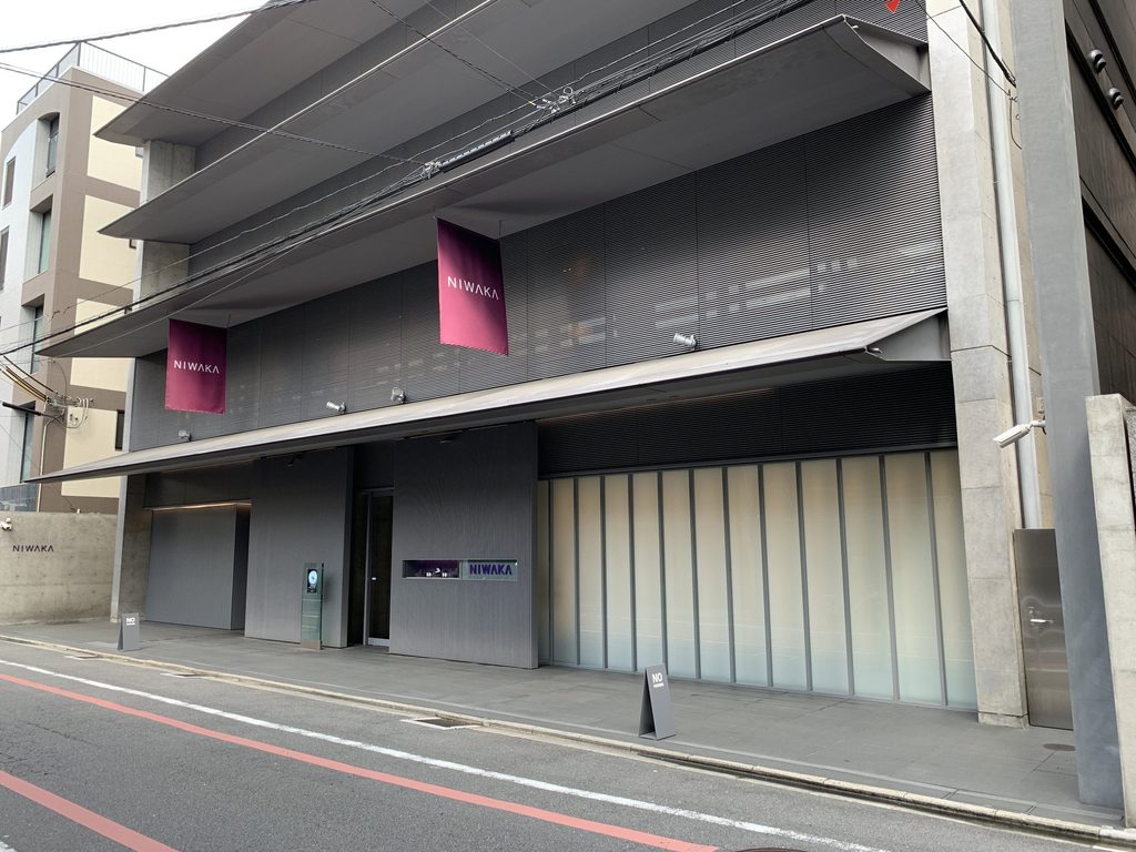 重なる屋根と深い庇、紫色の旗が見える俄ビルの外観 / Oblique exterior view of the NIWAKA Building with layered roofs, deep eaves and purple banners