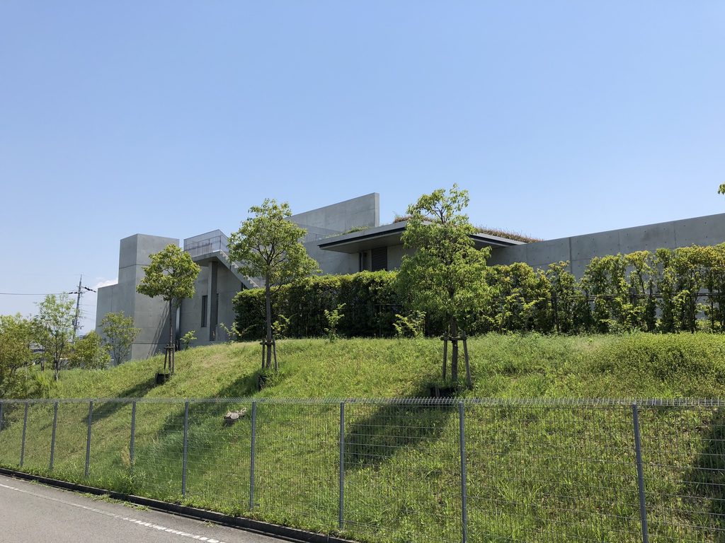緑の斜面からコンクリート壁が立ち上がる老木レディスクリニック2 / Concrete walls of Oiki Ladies Clinic 2 rising above the green slope