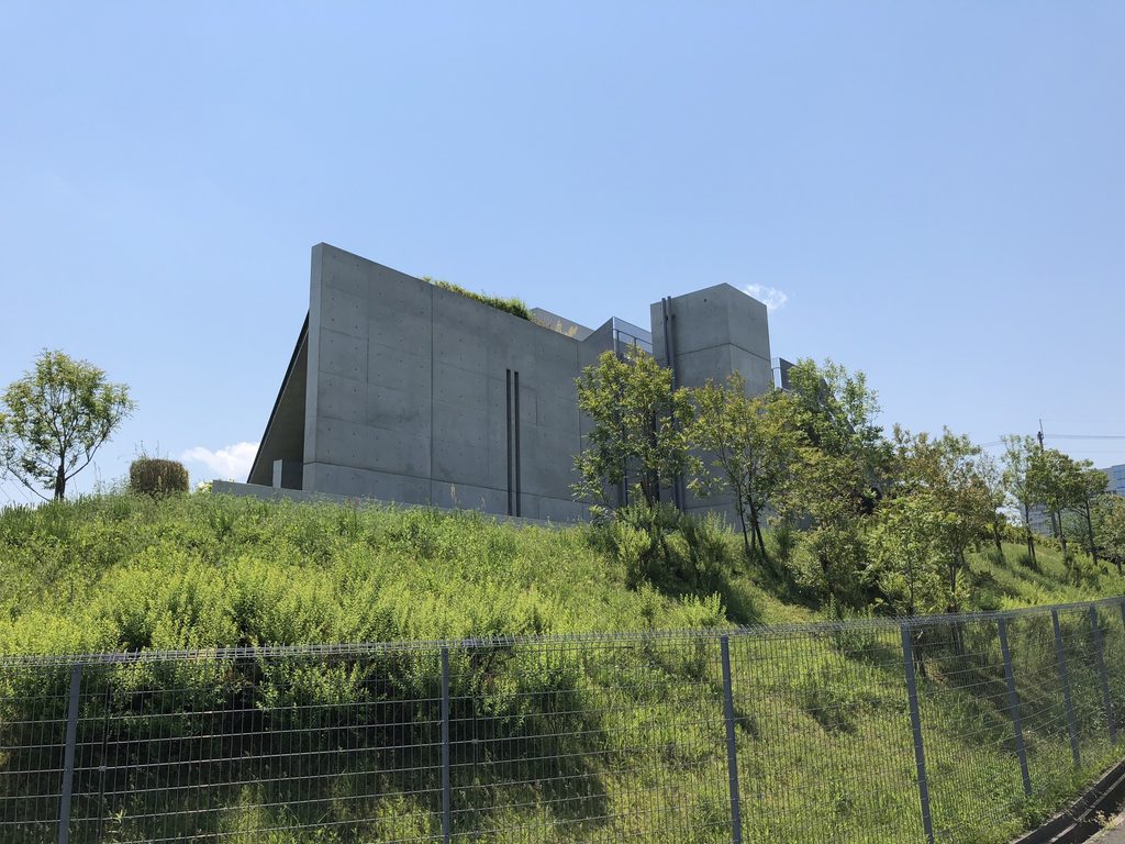 斜面上に立つ打放しコンクリート壁を見上げた老木レディスクリニック2 / Exposed-concrete wall of Oiki Ladies Clinic 2 rising above the slope