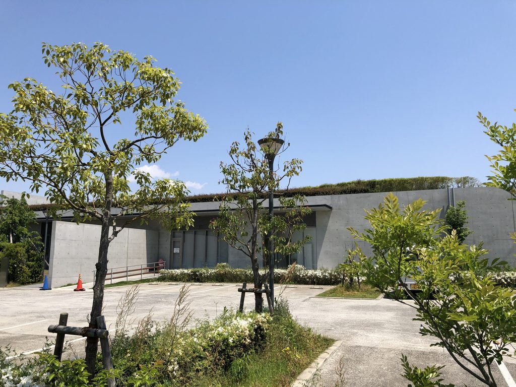 樹木の間から低い屋根とガラス面が見える老木レディスクリニック2 / Low roof and glazing of Oiki Ladies Clinic 2 seen through trees