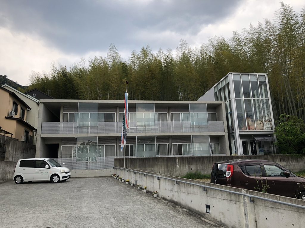 天王山の緑を背に建つ洛和グループホーム大山崎の全景 / Overall view of Rakuwa Group Home Oyamazaki against the greenery of Tennozan