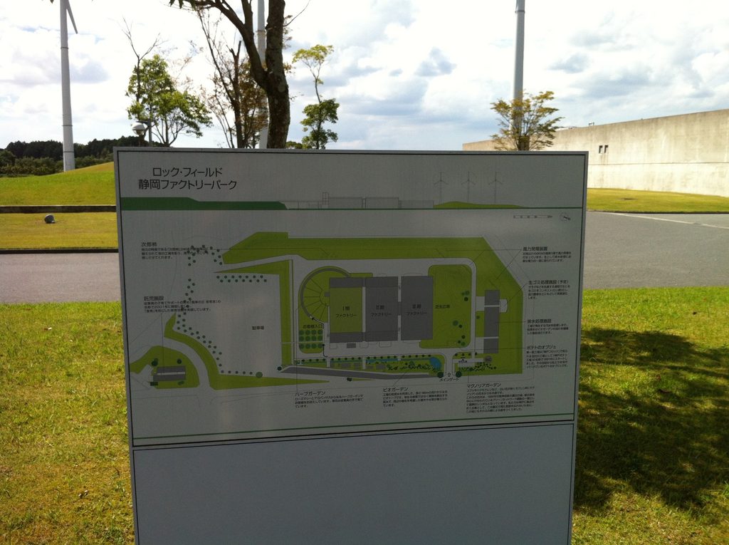 広い芝生の向こうに水平に伸びるロック・フィールド静岡ファクトリーの建物 / Long horizontal building of Rock Field Shizuoka Factory seen across the expansive lawn