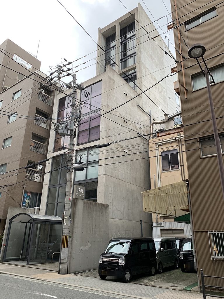 斜め下から見上げるSEASビルのコンクリート壁と上層部 / Concrete walls and upper volume of SEAS Building viewed obliquely from below