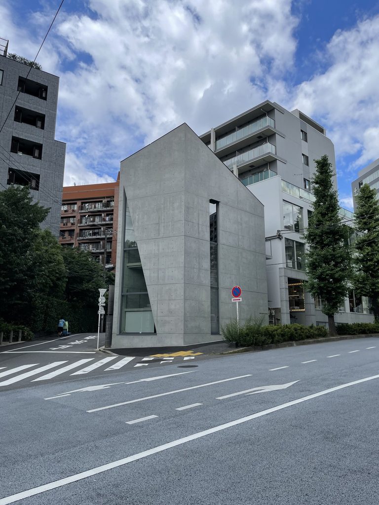 南青山の交差点から見たシマ・クリエイティブハウスの全景と斜めに立ち上がる打放しコンクリート壁
Overall view of Sima Creative House from a Minami-Aoyama junction, showing its sloping exposed-concrete profile