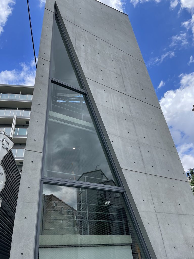 シマ・クリエイティブハウスの高いコンクリート壁を斜めに切り込む三角形のガラス開口
Triangular glazed opening cutting diagonally through the tall concrete wall of Sima Creative House