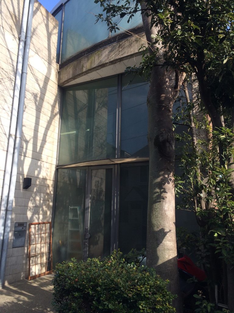 樹木と植栽越しに見る旧SUPER POTATO本社のガラス面 / Glazed facade of the former SUPER POTATO headquarters seen behind trees and planting
