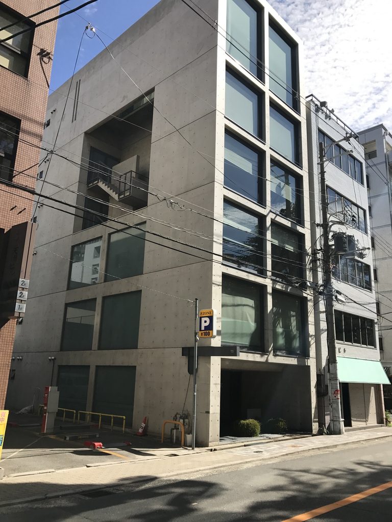 街角から見上げるTSビルの細長いコンクリート躯体と上部の開口 / Oblique view of the narrow concrete volume and upper opening of TS Building