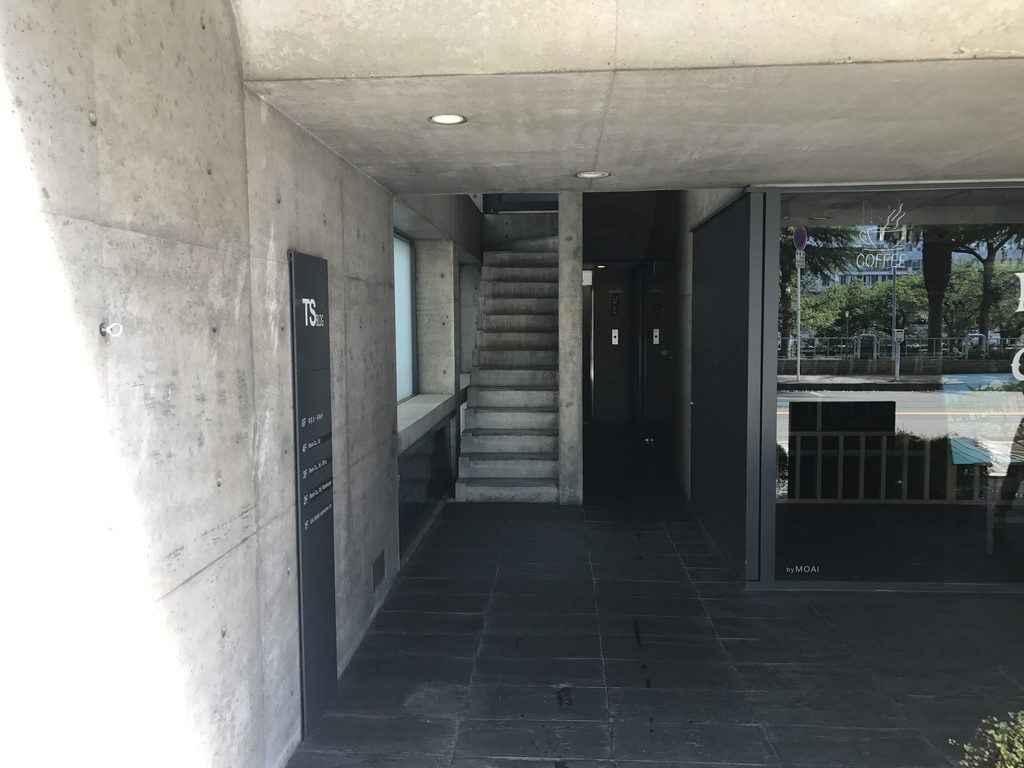 TSビル入口から見えるコンクリート階段と奥へ続く共用空間 / Concrete stair and shared passage visible from the entrance of TS Building