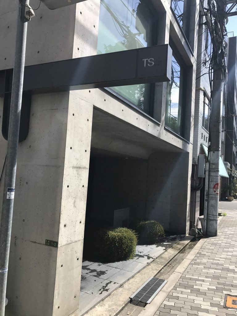街路へ突き出すTSビルの黒いサインと打放しコンクリートの柱 / Black TS sign projecting from the exposed-concrete facade of TS Building