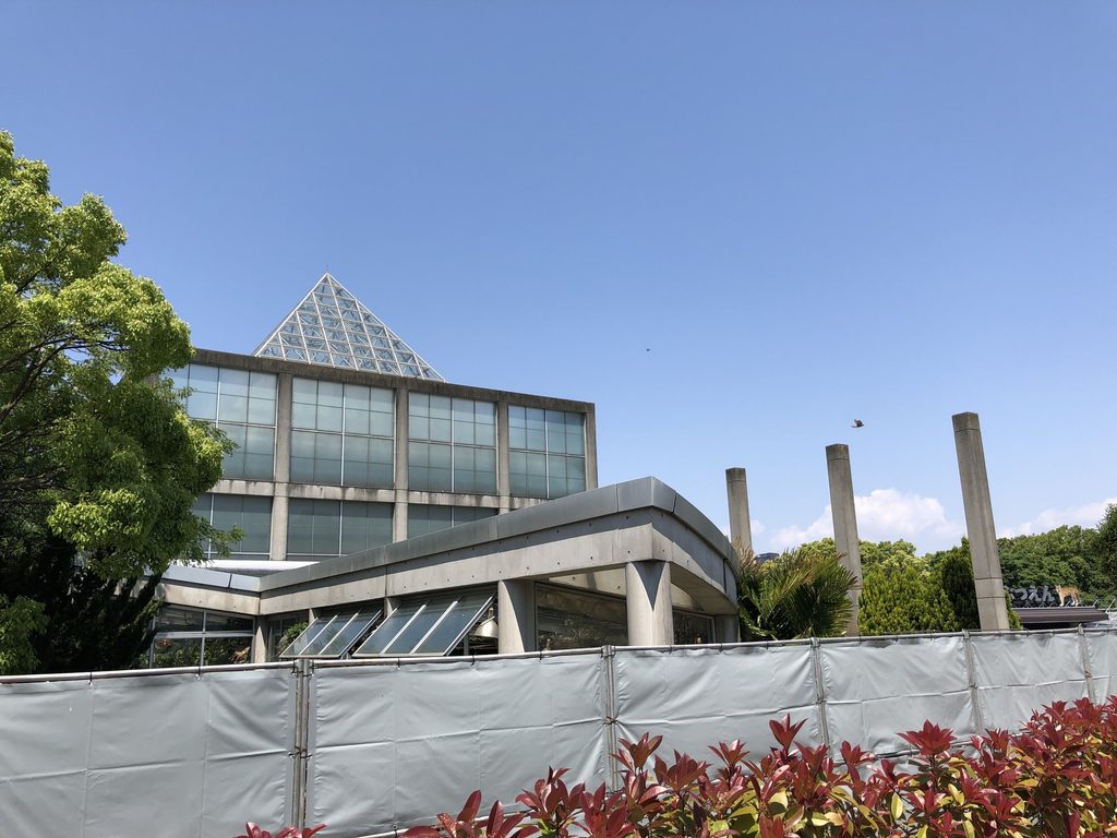 仮囲い越しに見る天王寺博覧会テーマ館の斜めの屋根と柱列 / Sloping roof and columns of the Main Pavilion for the Tennoji Fair seen beyond temporary fencing