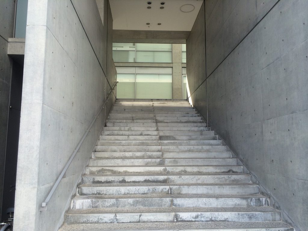 打放しコンクリート壁の間を上るTHE QOLの大階段 / Broad stair rising between exposed-concrete walls at THE QOL
