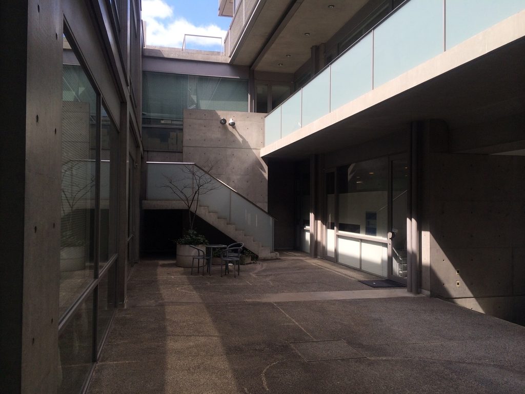 コンクリートとガラスに囲まれたTHE QOL低層部の外部空間 / Exterior space within the lower levels of THE QOL surrounded by concrete and glass
