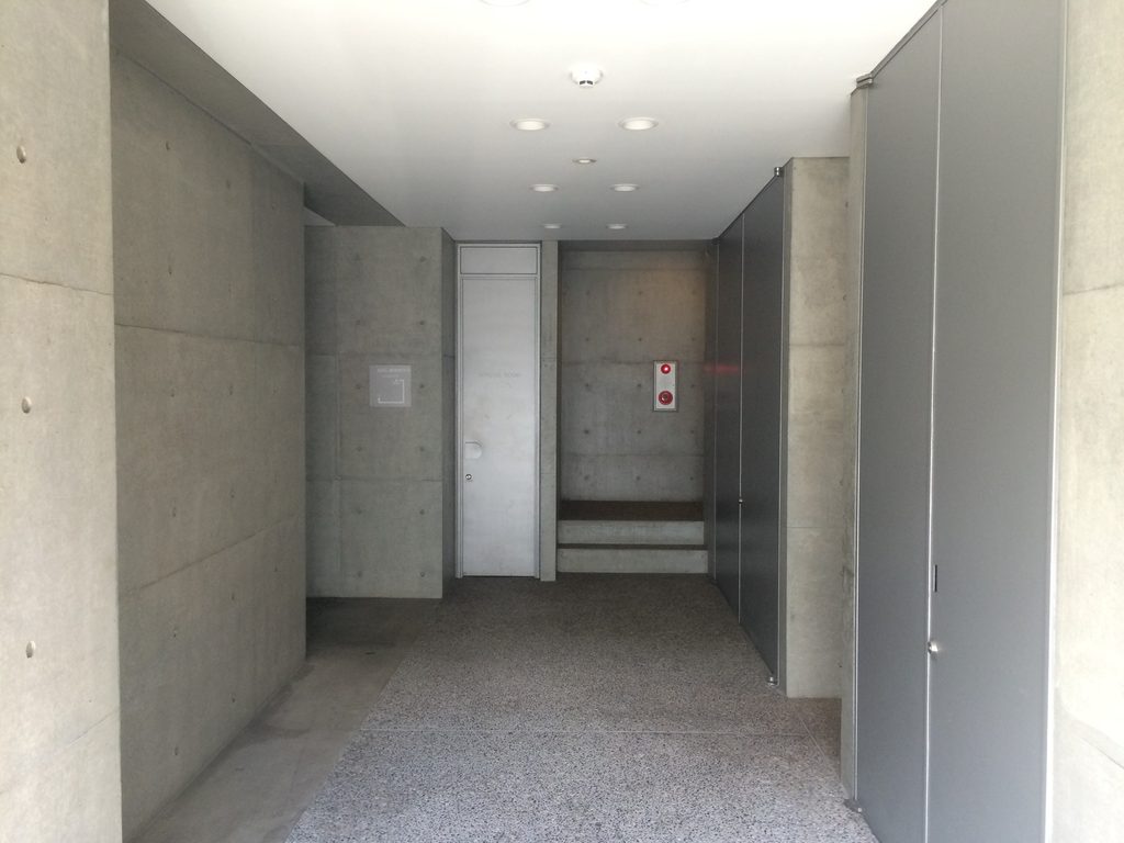 打放しコンクリート壁に挟まれたTHE QOLの共用通路 / Communal passage between exposed-concrete walls at THE QOL